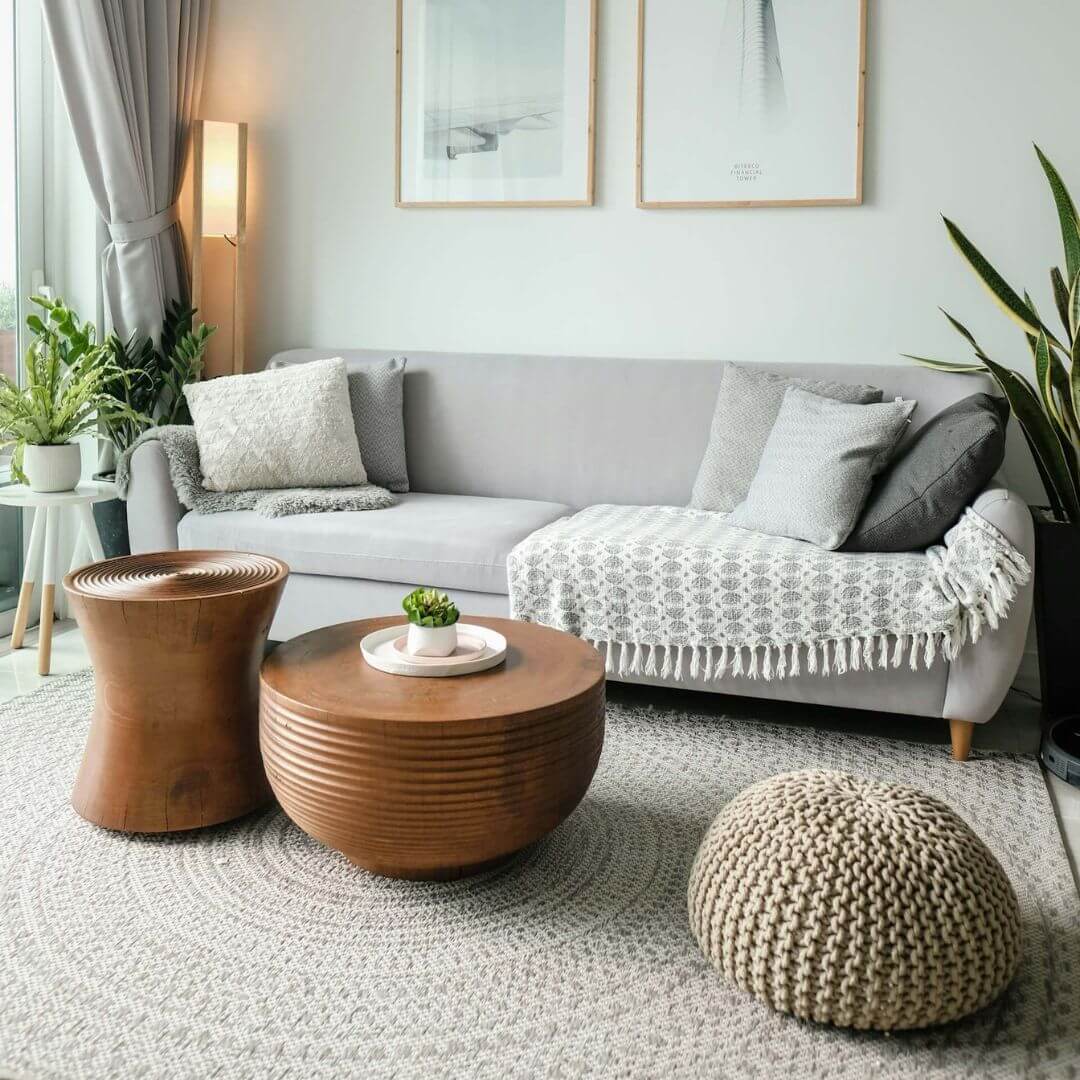 Boho-style living room furniture (couch, coffee table, pouf ottoman) with plants to the side of the couch and two pictures on the fall behind the couch