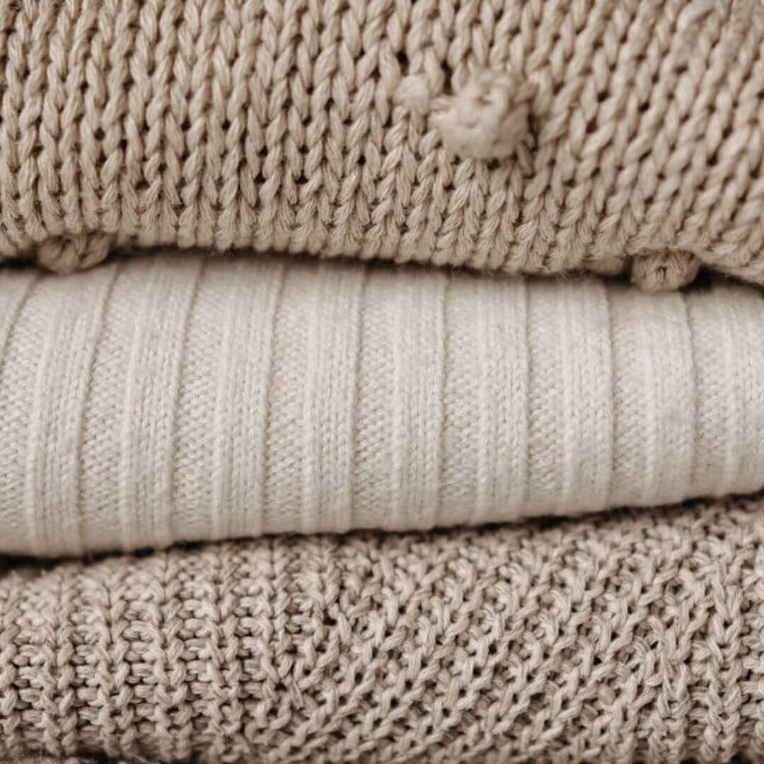A close-up of folded beige and tan sweaters