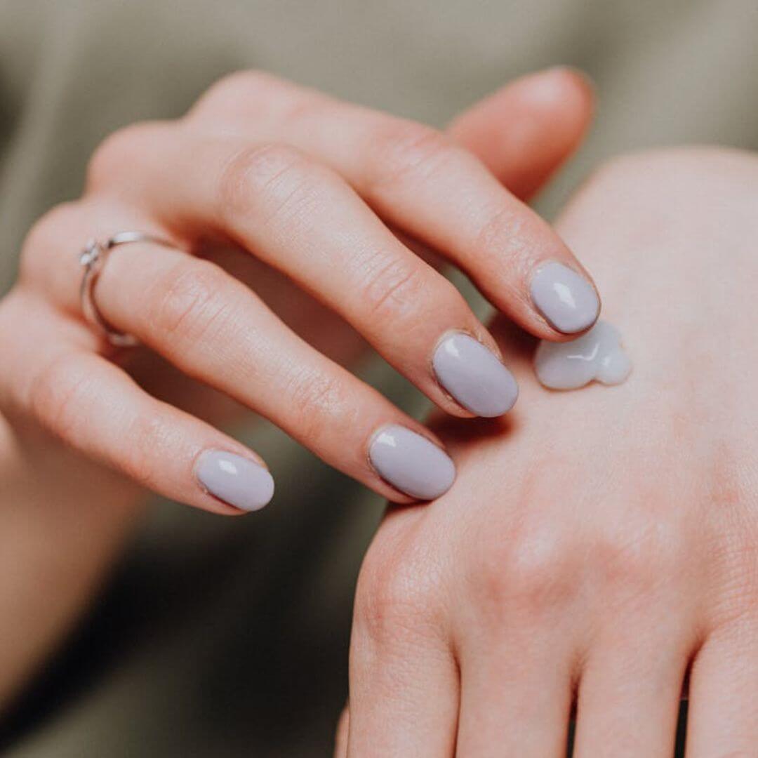 A close-up of a woman's hand; she has light lavender nail polish and is putt a small dot of lotion on her hand