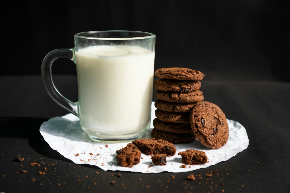 Tall glass of milk with a stack of chocolate chip cookies on a dark background. (Photo Credit: Mirza Mustofa)