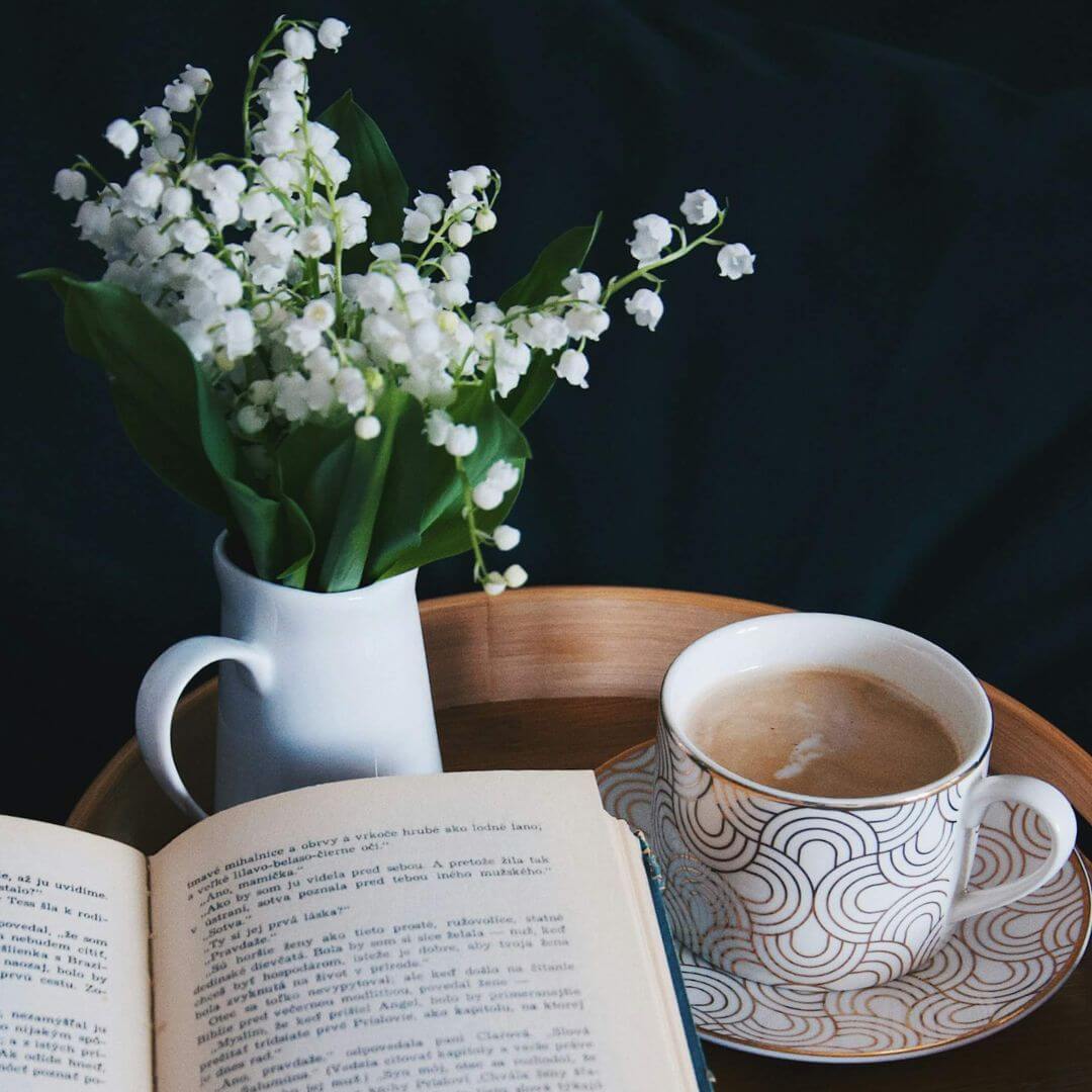 Open book with a cup of coffee to the right and flowers behind it (square)