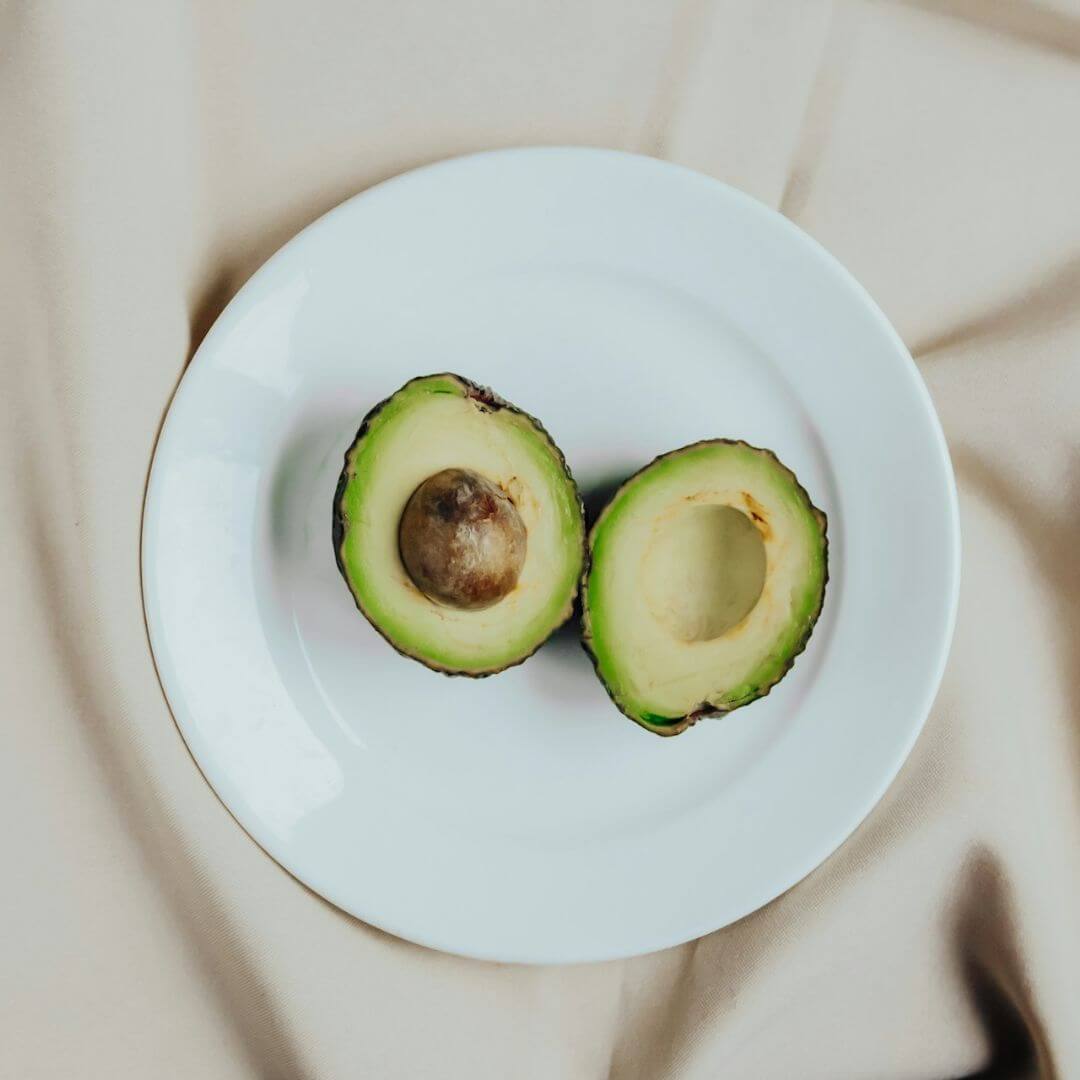 A white plate with an avocado sliced in half and open