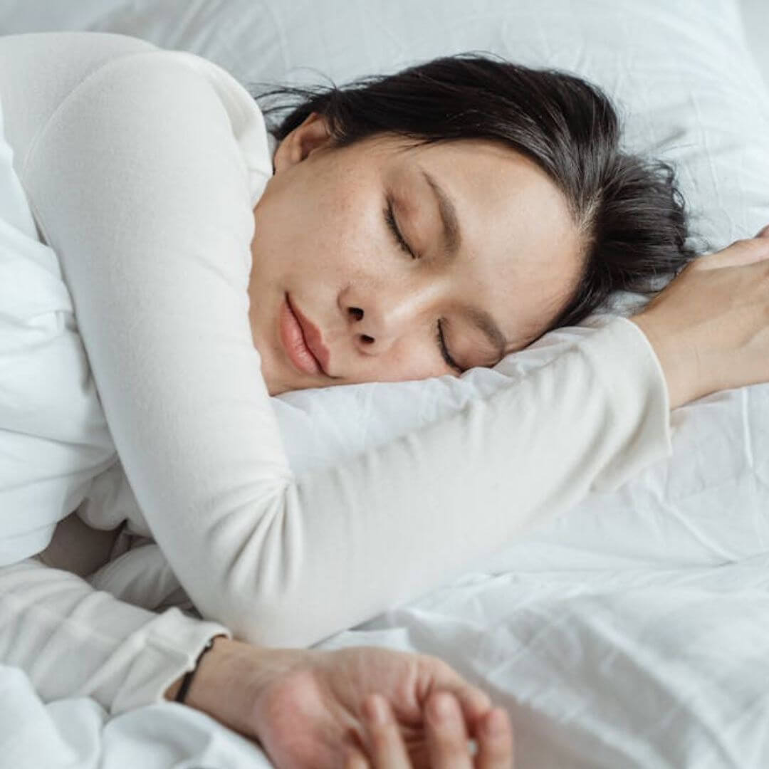 A woman with dark hair sleeping on her side with her arm by her face