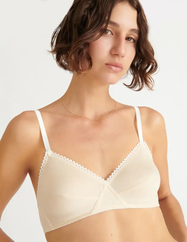 A woman wears an undyed organic cotton triangle bra by Araks, featuring soft cups, delicate scalloped trim, and minimalist stitching. Designed in New York with sustainable materials and ethical production, the bra blends simplicity with luxury. (Photo Credit: Araks)